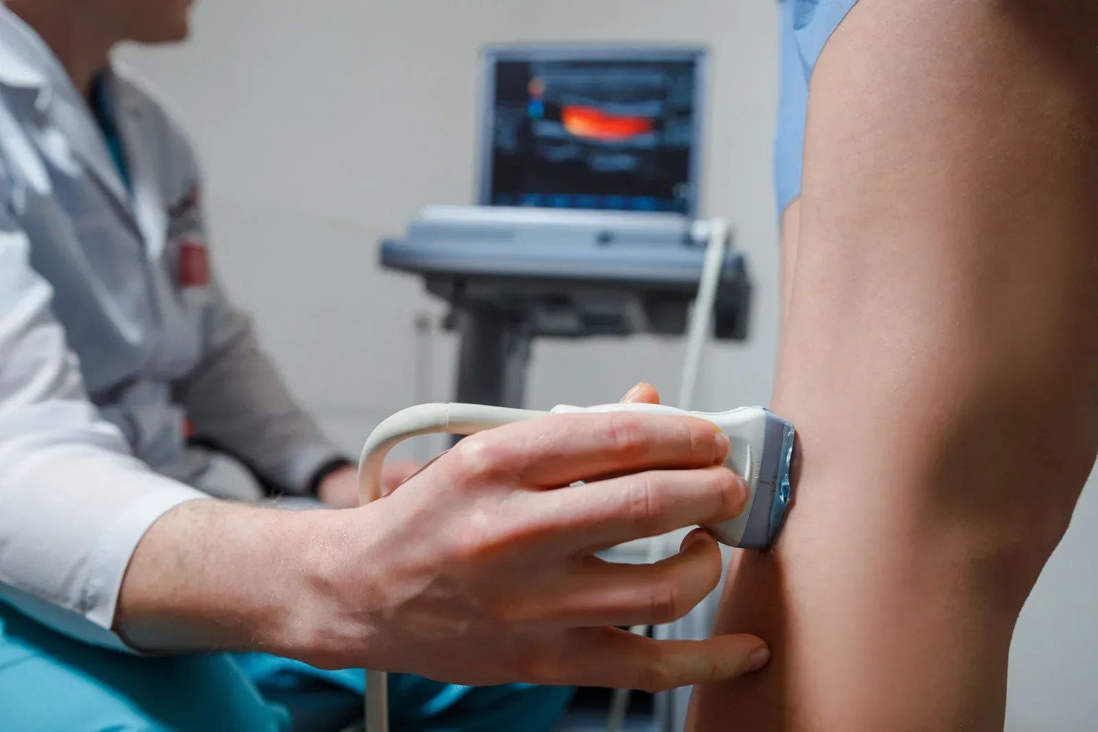 A Doppler ultrasound probe held against a patient’s leg, with the vessel image on the screen behind